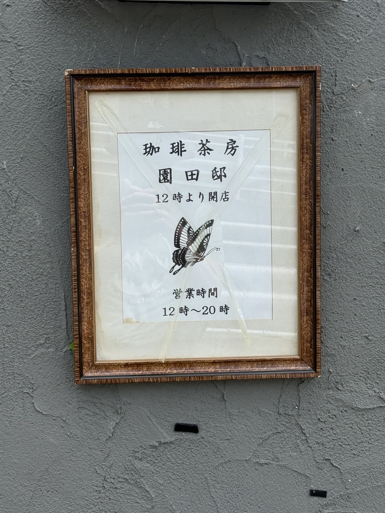 Framed sign outside 珈琲茶房 園田邸, with a butterfly drawing and hours from noon to 8 p.m.